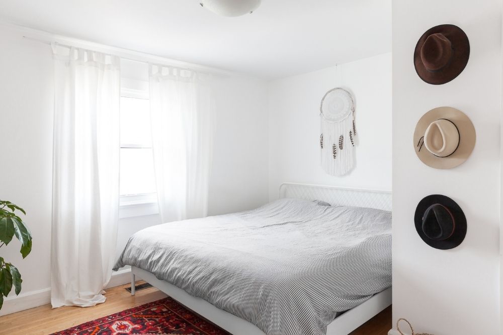 white bedroom with hats on wall and art above bed