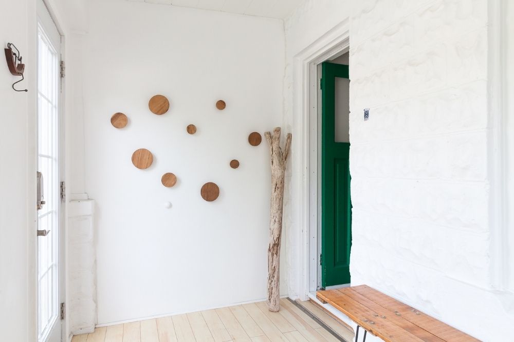 white front entryway porch with round wooden hooks on wall, standing branch and wooden bench