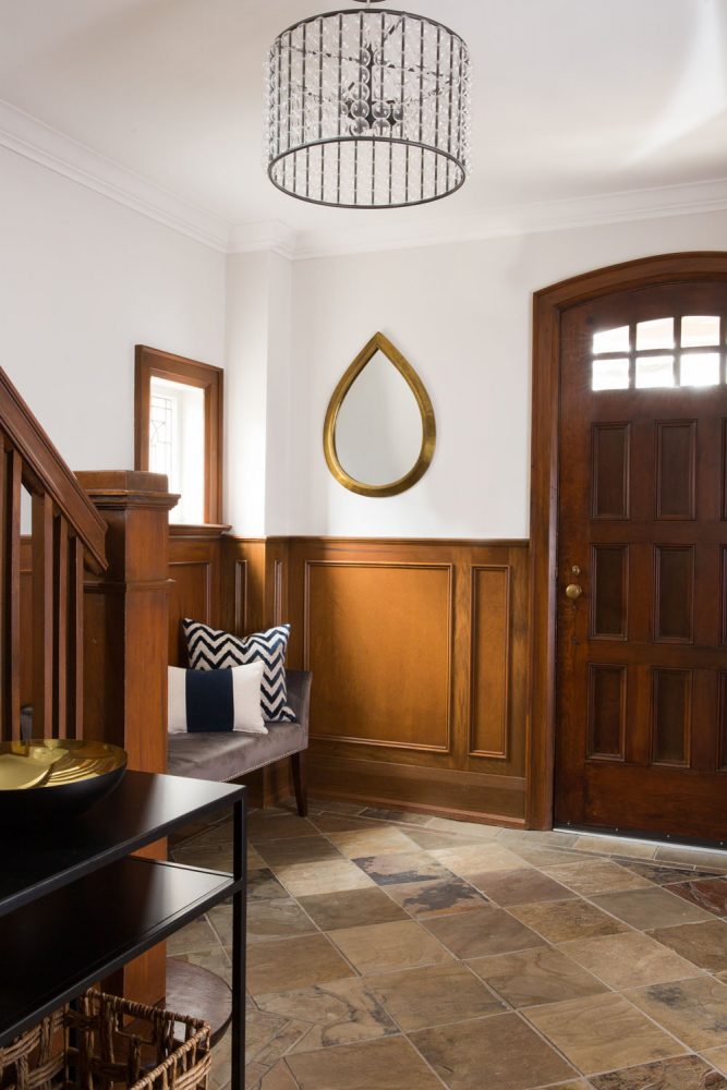 front wooden door and hall with wood wainscotting and teardrop mirror on upper white wall
