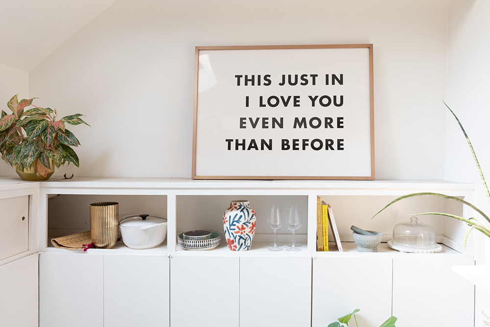 Kitchen shelving with artwork that says: I love you even more than before.