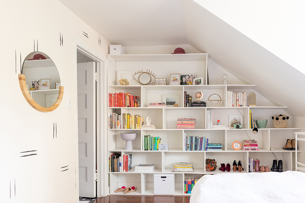 Bedroom with entire wall white bookshelf with books colour coded