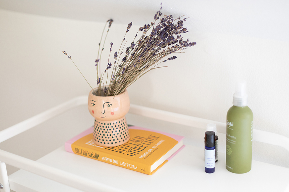 White nightstand with air freshener, books and lavender sitting on top