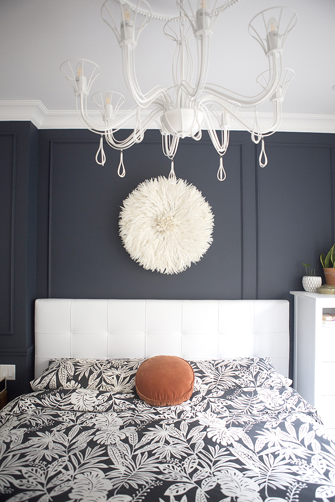 Bedroom with dark grey wall, floral graphic bedspread and white chandelier hanging above