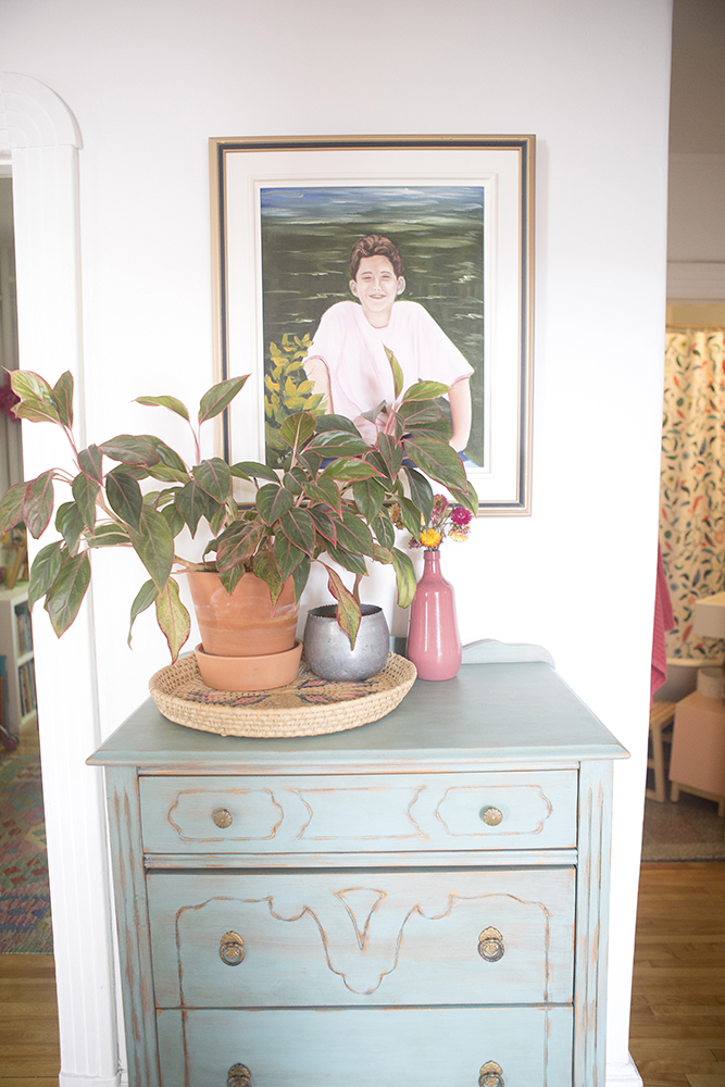 Closeup of blue dresser with plants and artwork on top