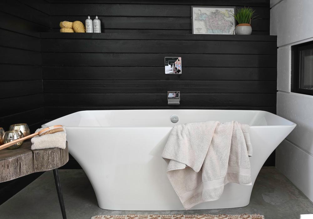 white vessel tub with towel over the side in front of black wall