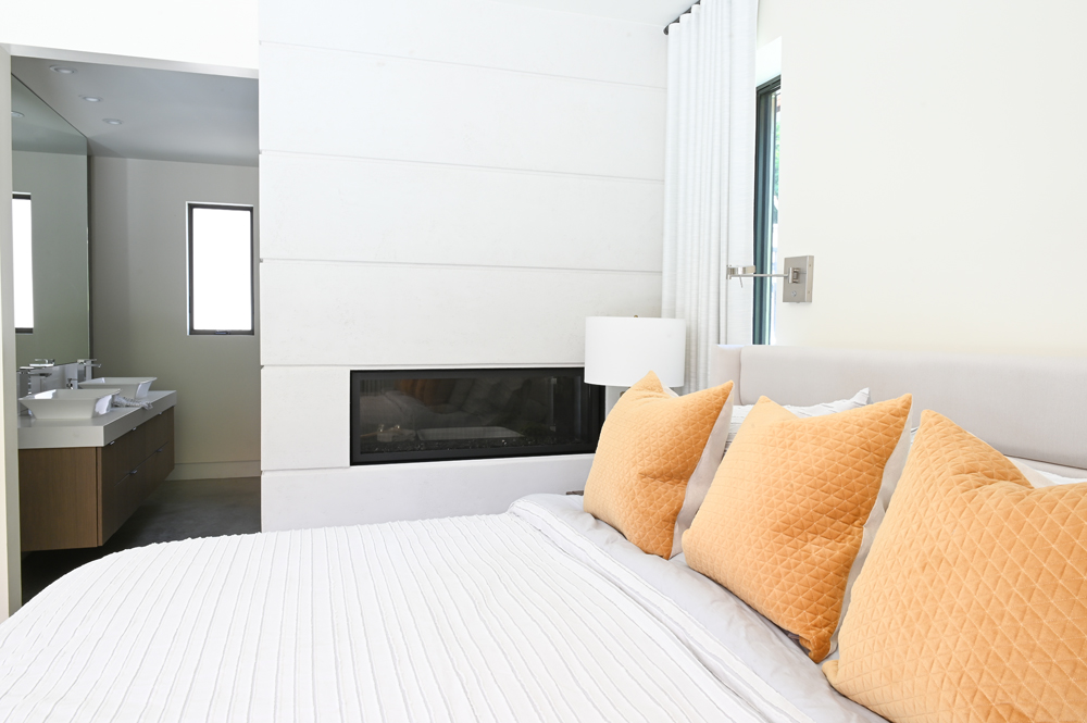 modern fireplace in master bedroom with three orange pillows and en suite bath