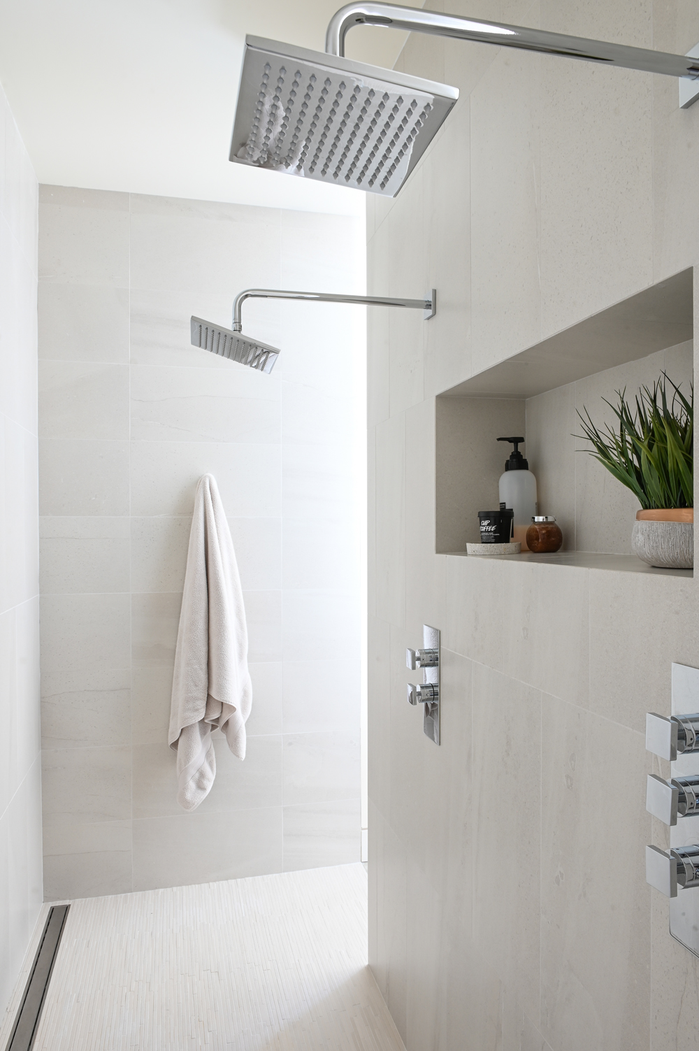 shower stall with two square chrome showerheads, towel hanging on hook