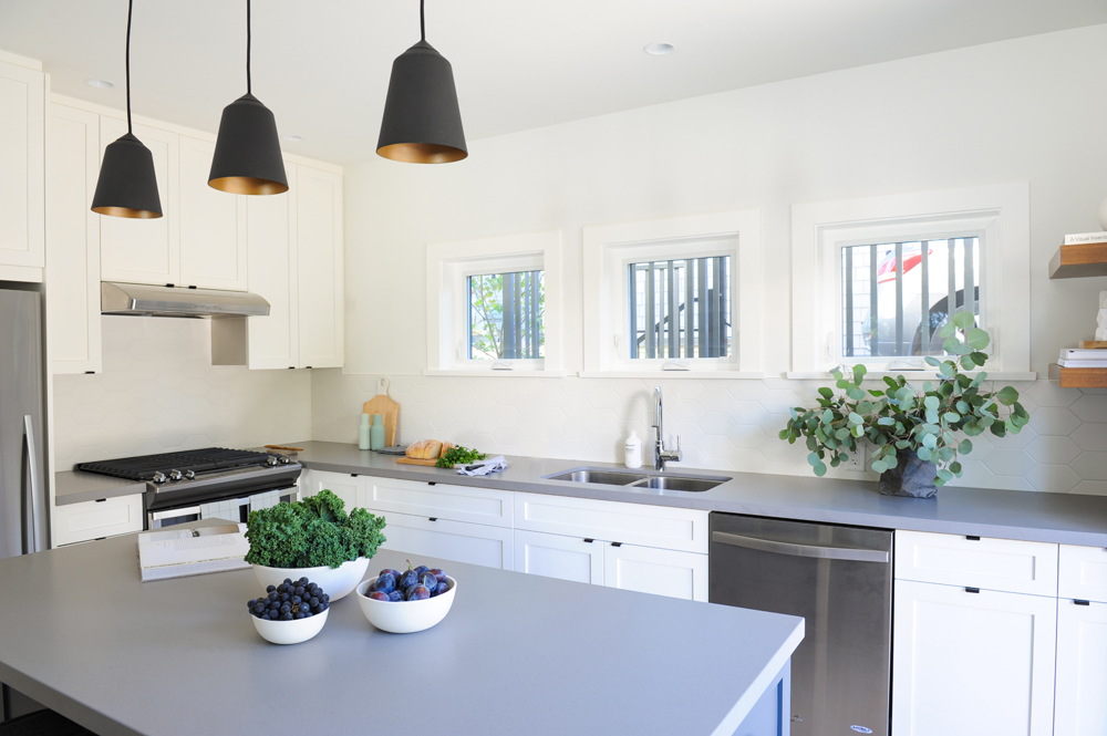 A narrow renovated kitchen with pale grey and white cabinetry and plenty of natural light