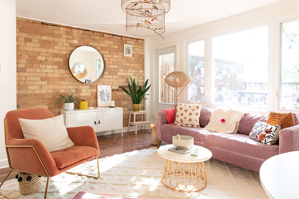 A renovated living room with an exposed brick wall, potted plants and pink furniture and decor
