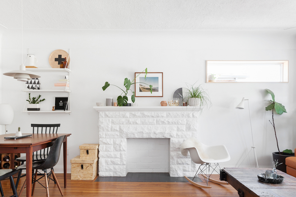 A white living room space with an unused fireplace with plants on the mantle