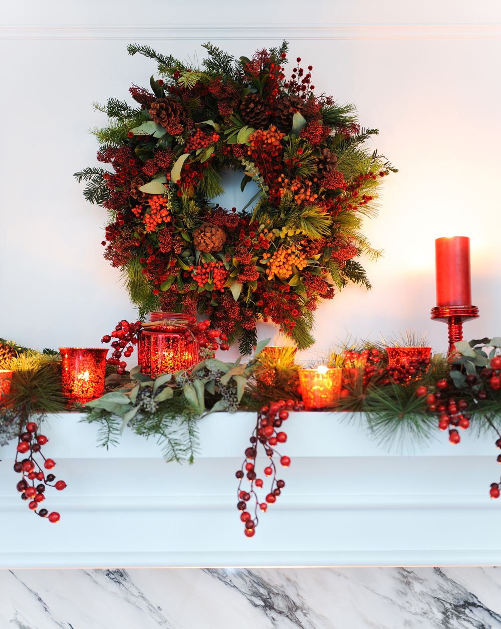 Red candles and evergreen on a marble mantelpiece