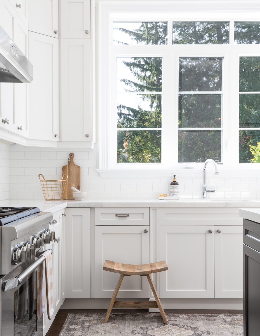 white kitchen, window, sink, wooden stool in front of cupboard
