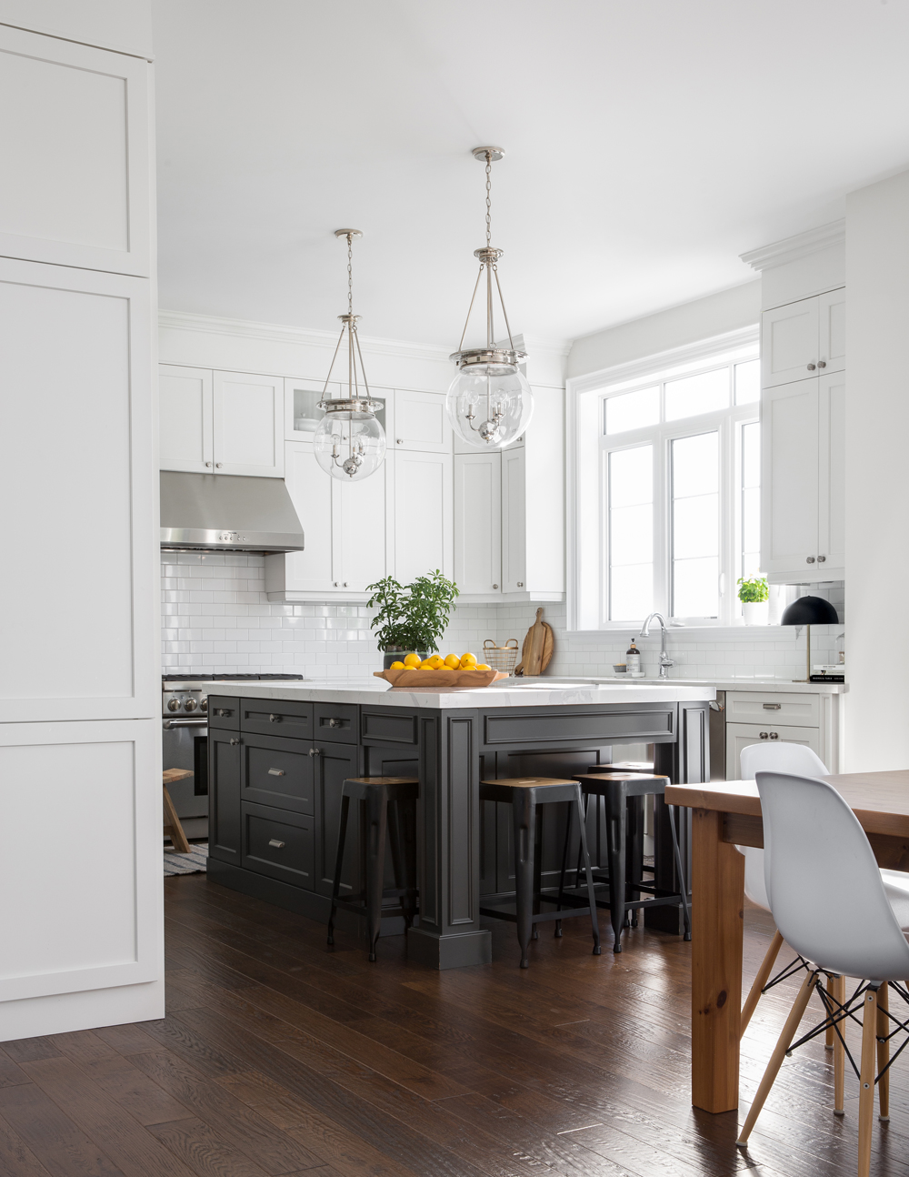 white kitchen with black based island, backless stools, wooden vessel filled with lemons on island