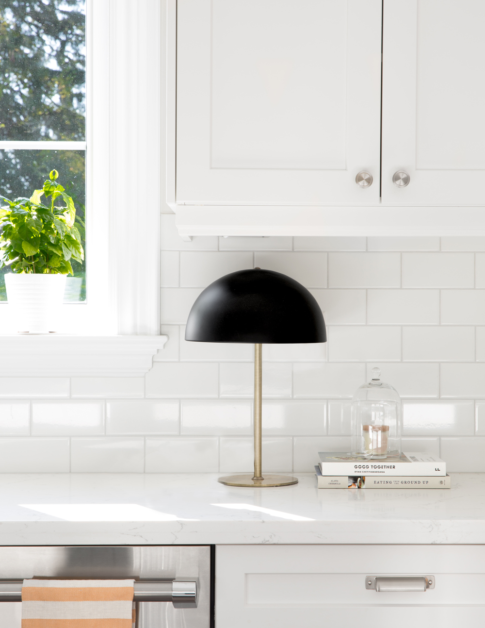 black shade lamp with brass stem on white kitchen counter with two books and white subway tiles