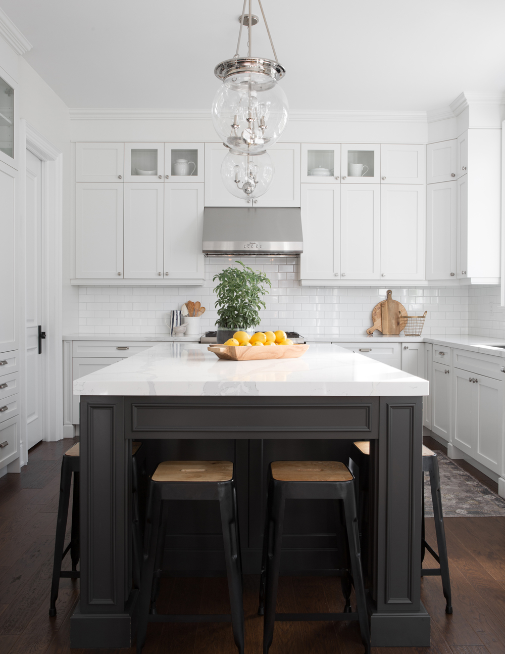 white kitchen with black-based island seen from side, stools beneath, lemons on top