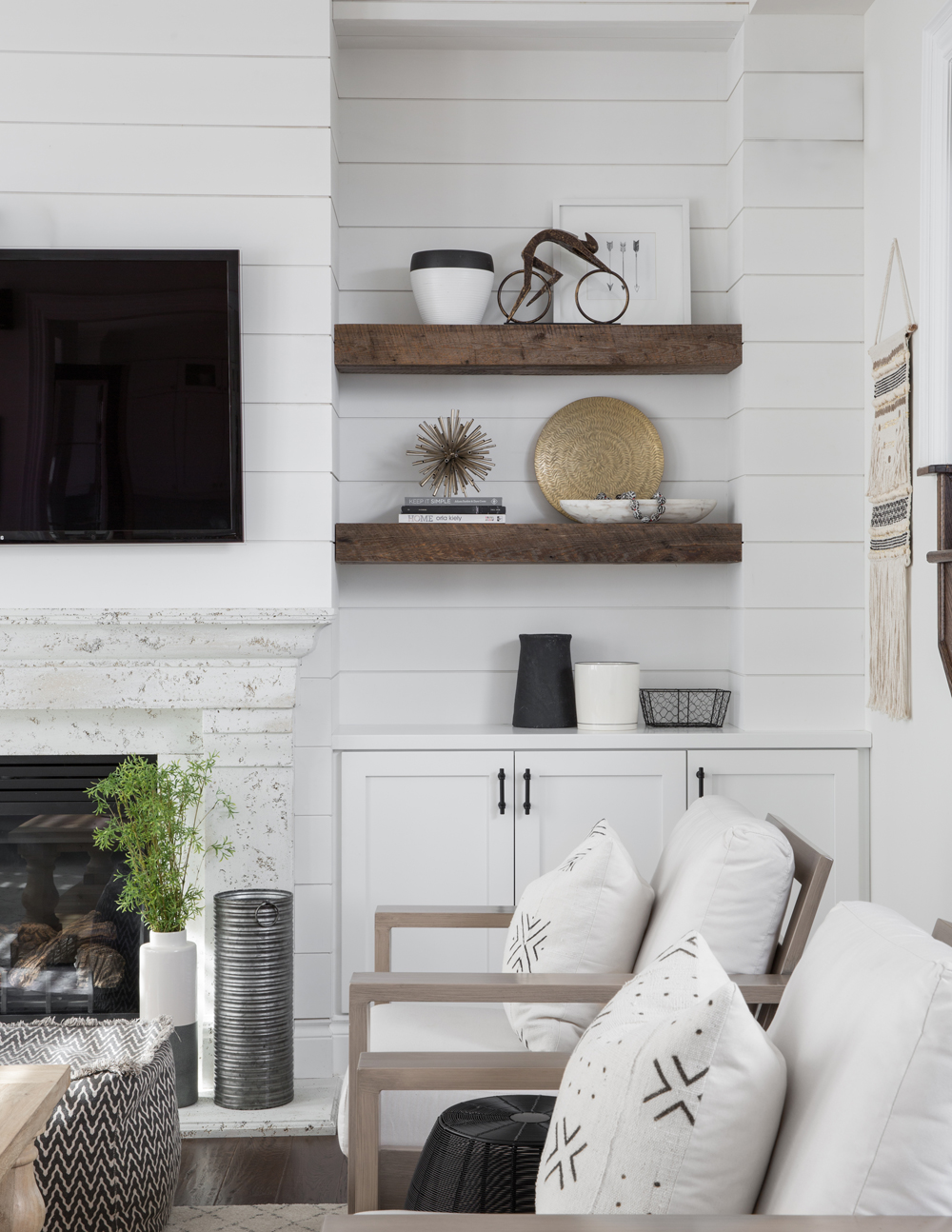 two wood floating shelves beside TV and fireplace, black rim white pot left on top shelf