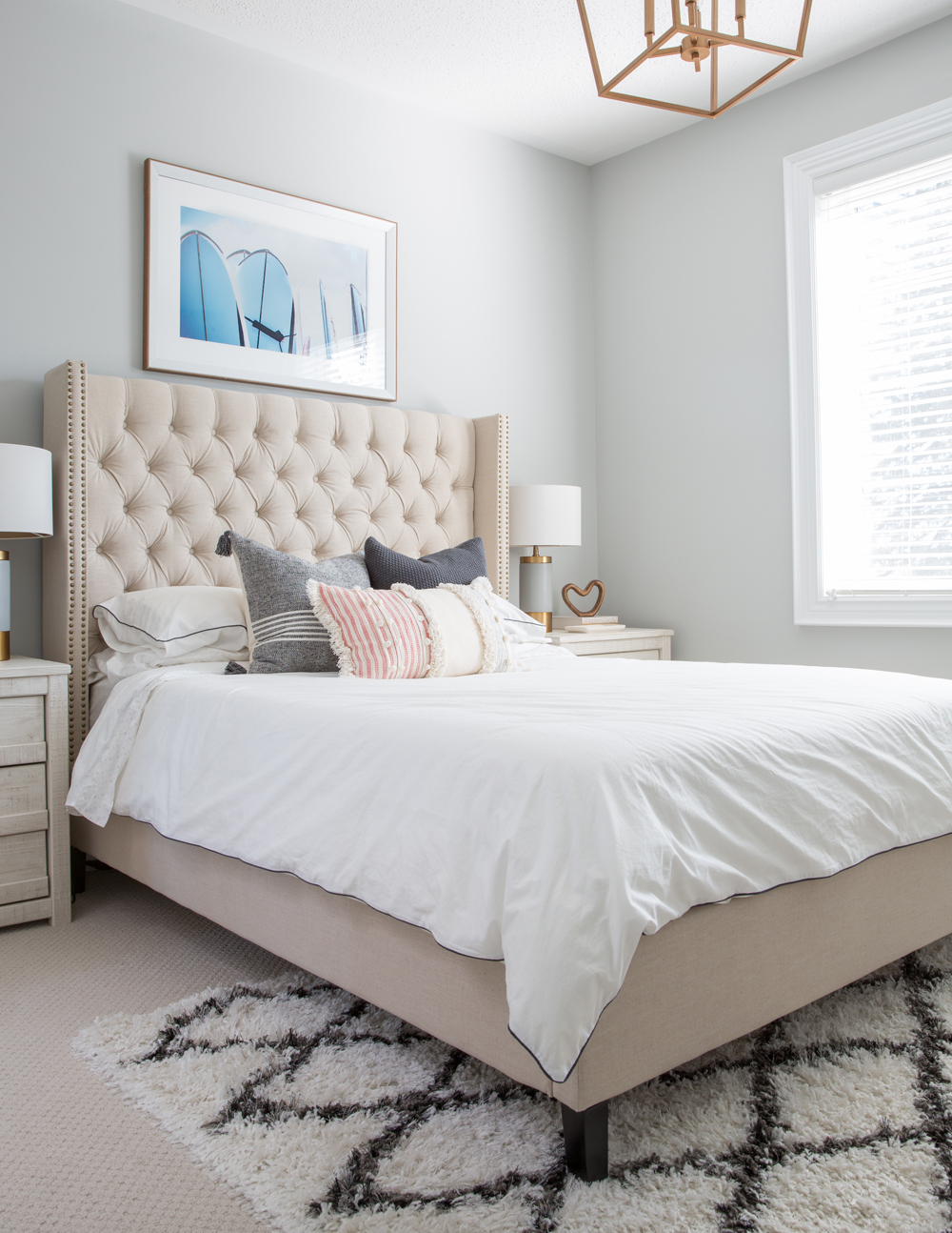 pink tufted headboard, blue framed art above, black and white area rug over wall to wall carpet