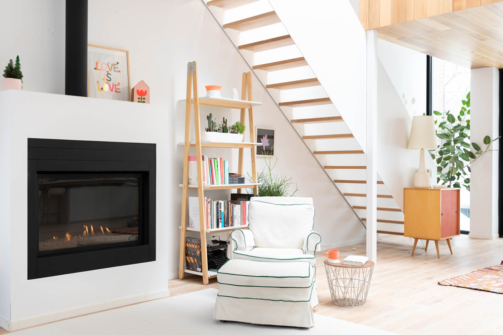 A minimalist white open-concept living room with a gas fireplace and open shelving with books and decor