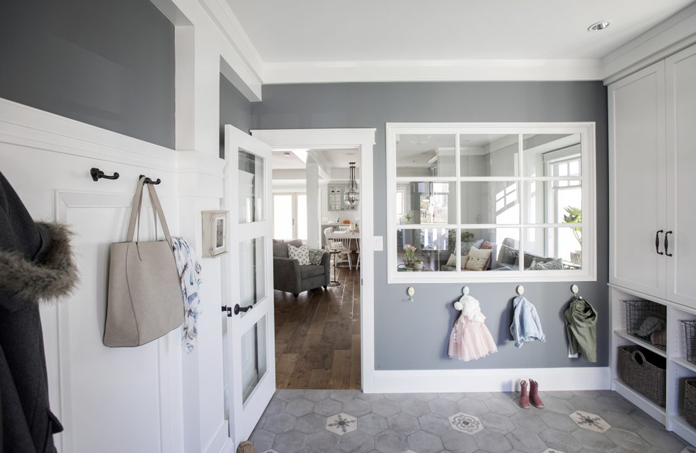 A grey and white spacious mud room with a window overlooking the living room and plenty of storage space