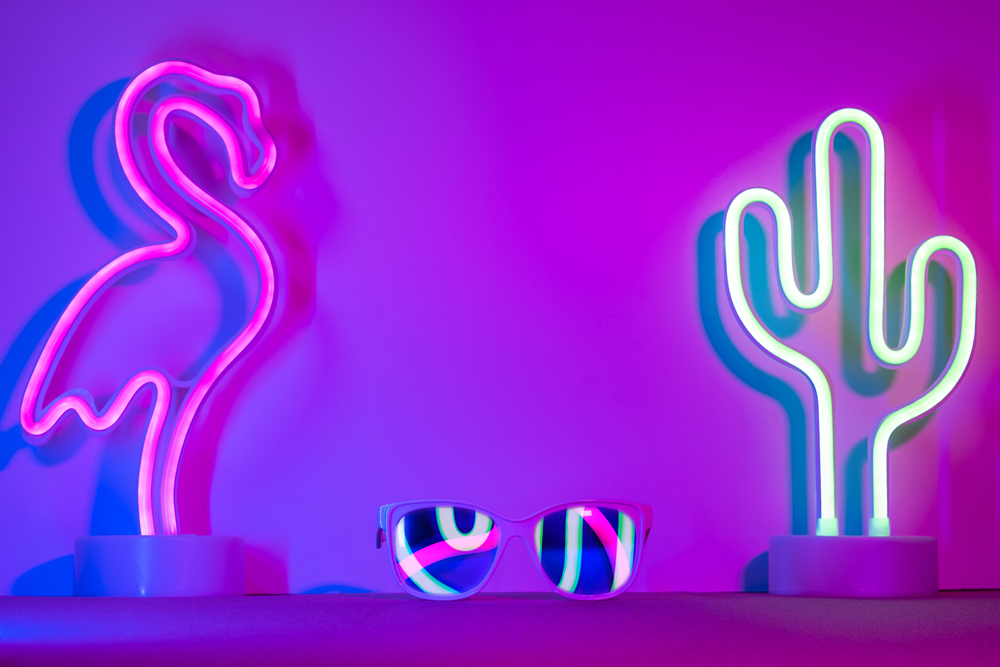 Neon signs of a pink flamingo and green cactus on a bedroom shelf between a pair of sunglasses