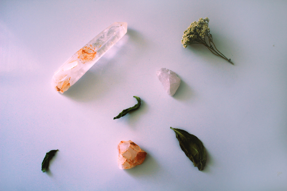 A variety of healing crystals and herbal leaves against a white background