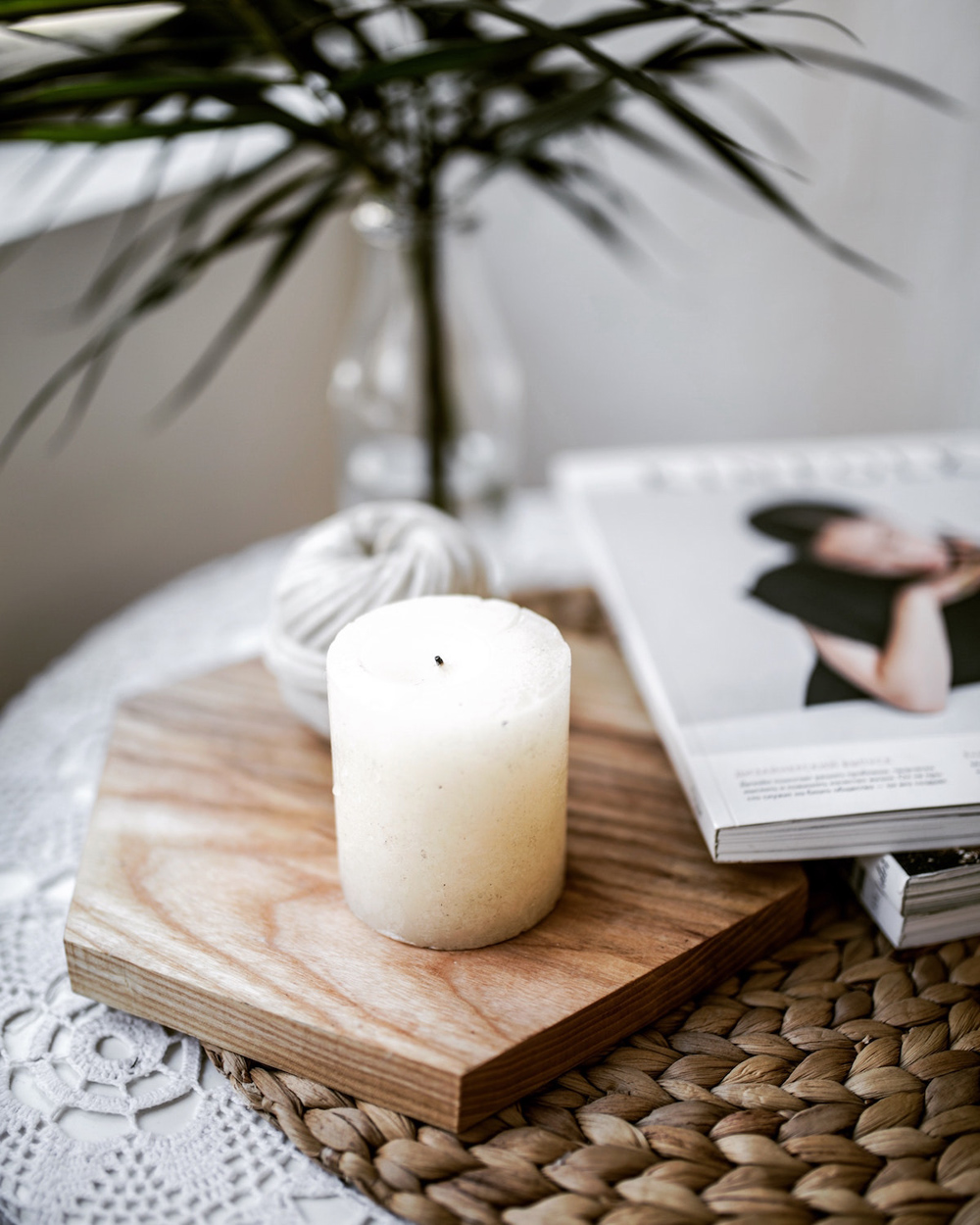 A scented candle on a block of wood placed on a coffee table near books and magazines