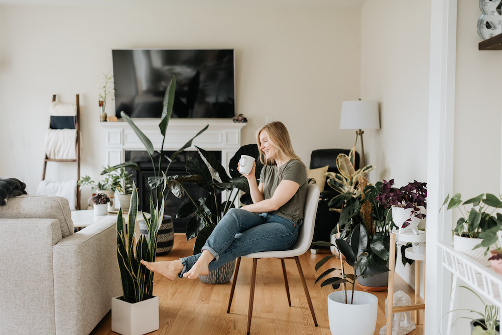 woman in white living room filled with green indoor plants