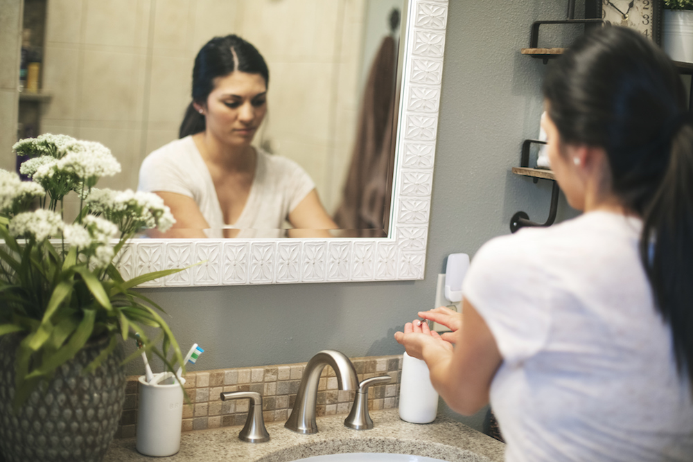 woman washing her hands in front of mirror at bathroom sink