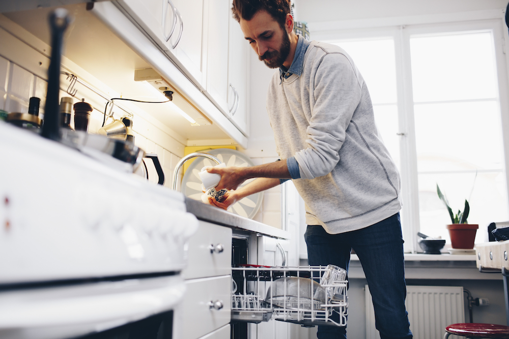 man putting utensils in dishwasher