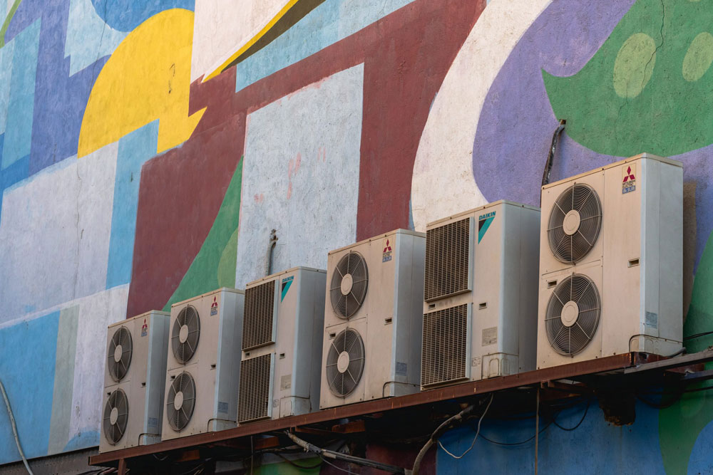 A row of air conditioning units installed on outside of a colourful building.