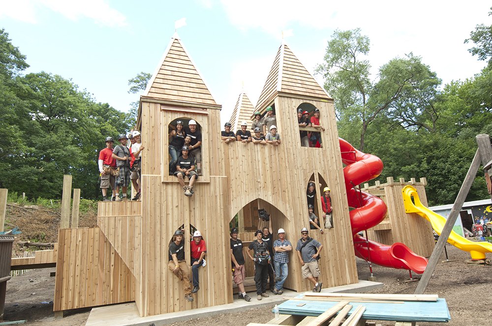 Mike Holmes and his team standing in a playground on a wooden tower