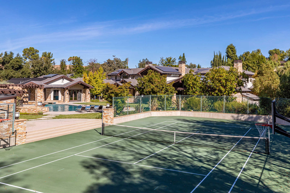 The tennis court, with a nearby basketball hoop, off to the side of the swimming pool