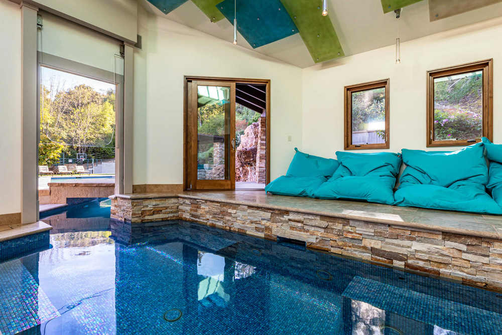 An indoor pool that boasts a tiny bridge that leads into the bigger backyard pool