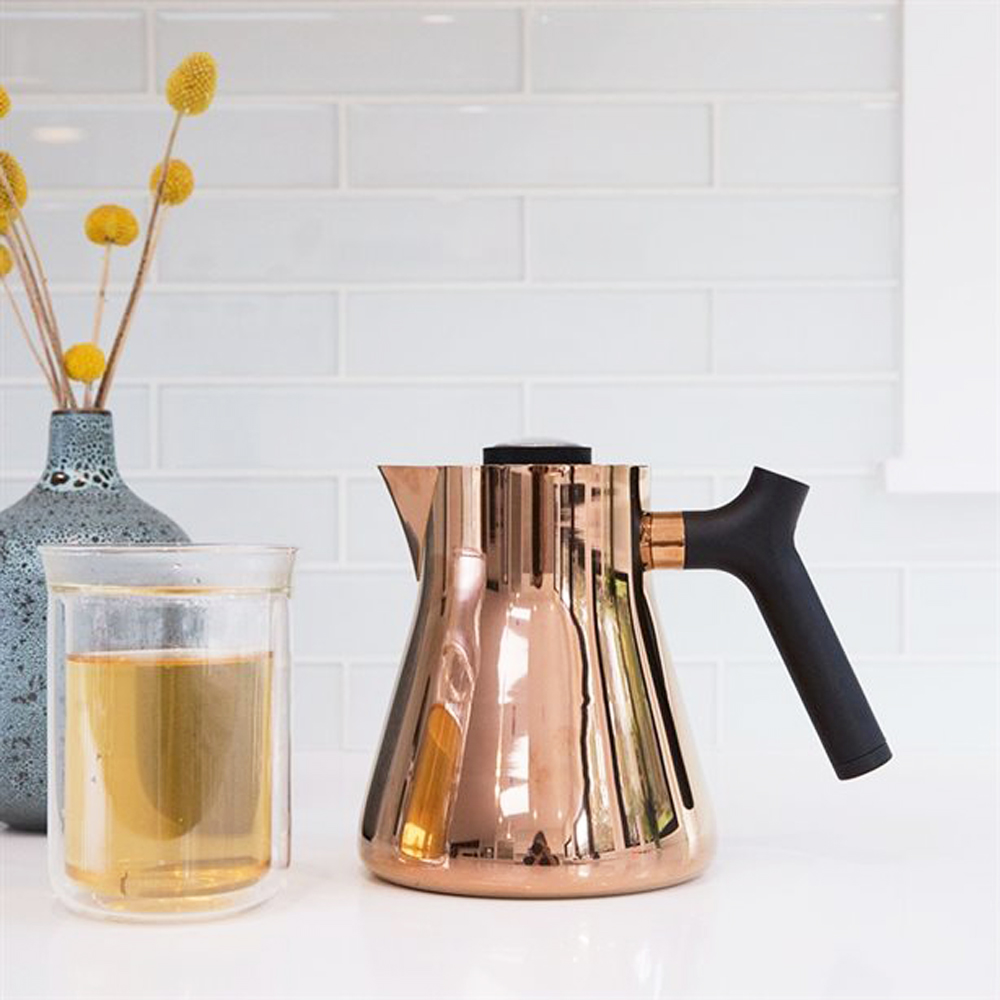 A rose-copper coloured stovetop kettle on a kitchen counter next to a mug of steeped tea