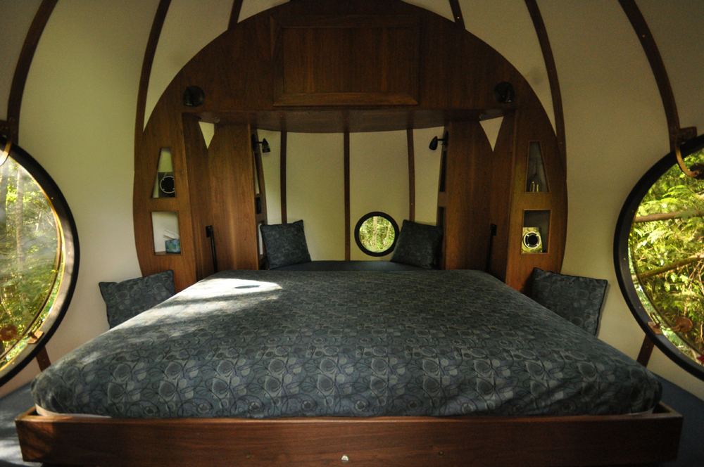 Interior of the Free Spirit Spheres, featuring a large bed with circular windows overlooking the trees