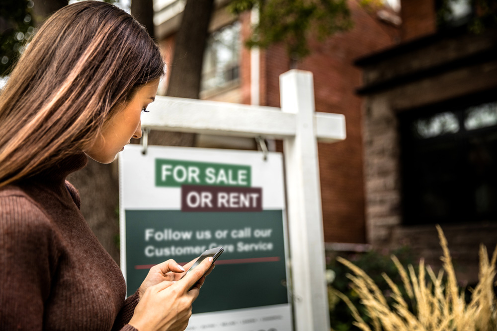 Woman looks at a for sale or rent sign
