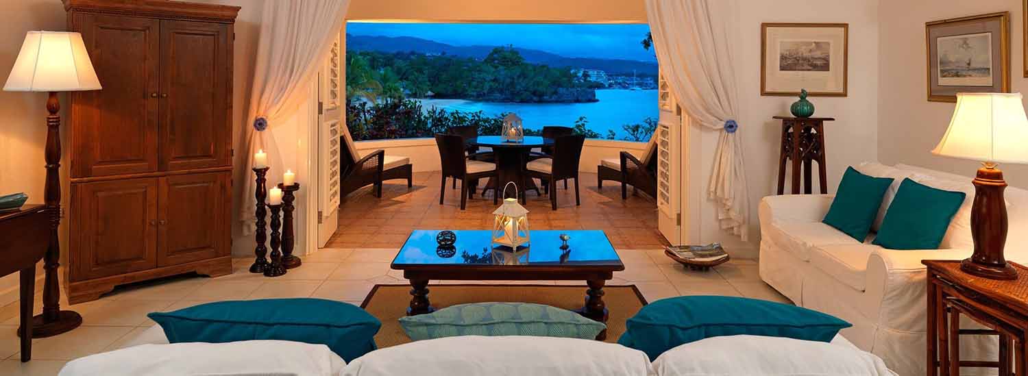 white room seen from behind three cushion sofa overlooking deck with blue ocean and scenery in background