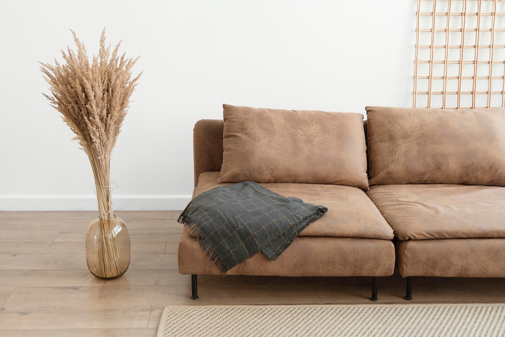 white living room with brown leather couch and dried fronds in vase