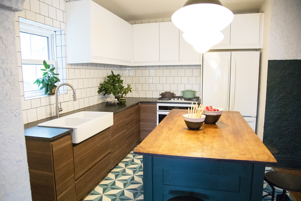 A tiny renovated kitchen with patterned floor tiles, wood and blue island and wood cabinetry with an apron sink
