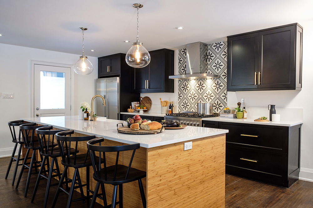 A black and white kitchen with a long marble and wood island with black chairs