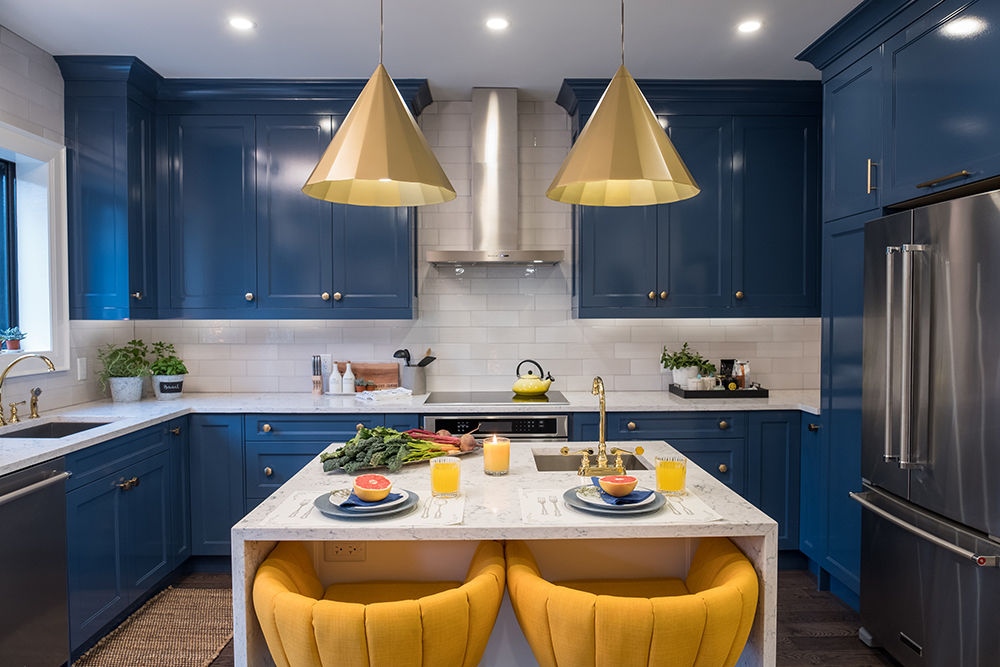 A bright blue renovated kitchen with a tiny white marble island surrounded by yellow-cushioned chairs
