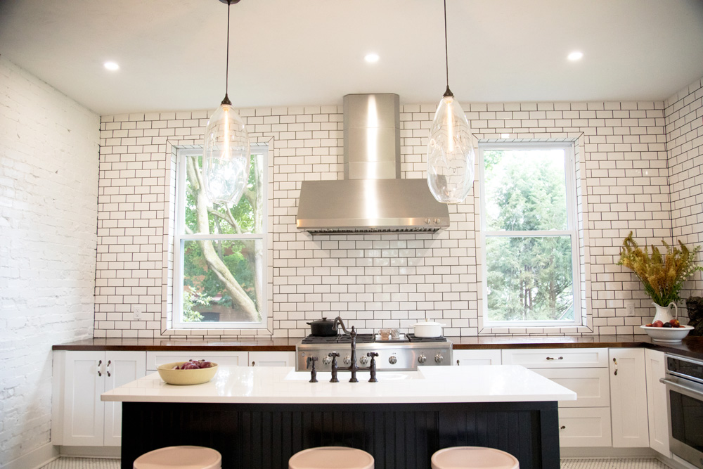 A pale pastel-hued kitchen renovation with oversized light fixtures, black and white islands and backsplash