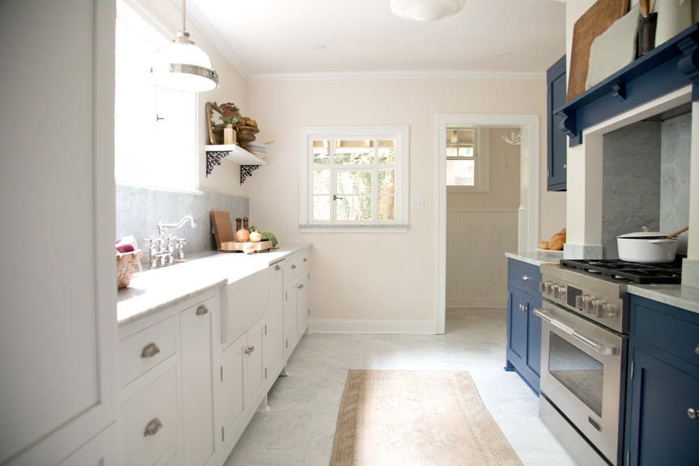 A blue and white narrow renovated kitchen with lots of natural light and floating shelves
