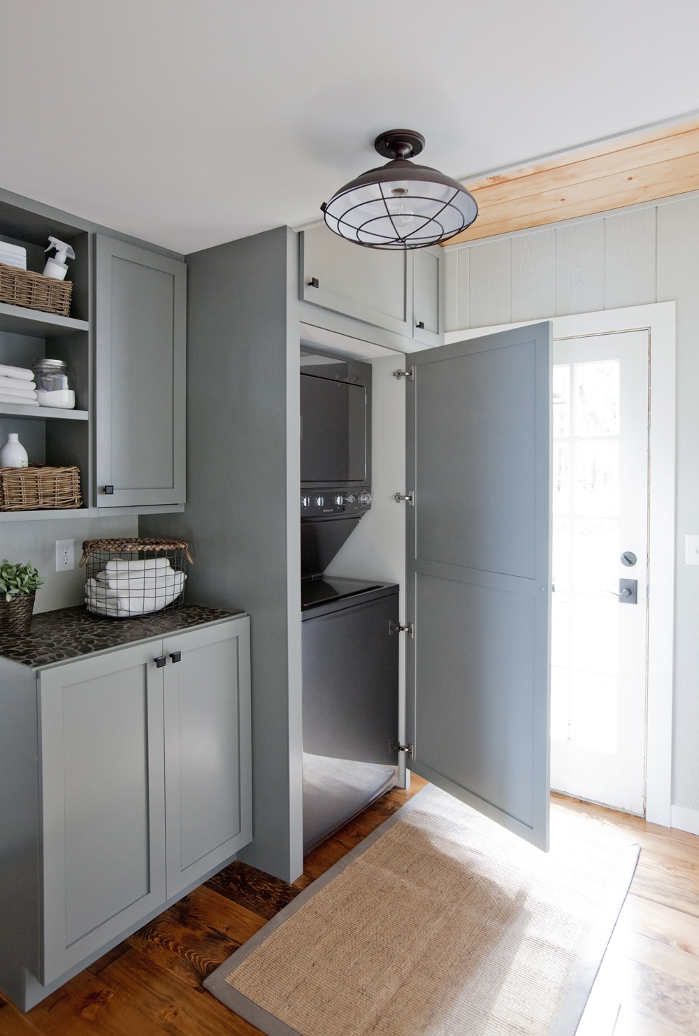 Bright laundry room with grey-blue custom cabinetry and washer and dryer concealed behind cupboard.