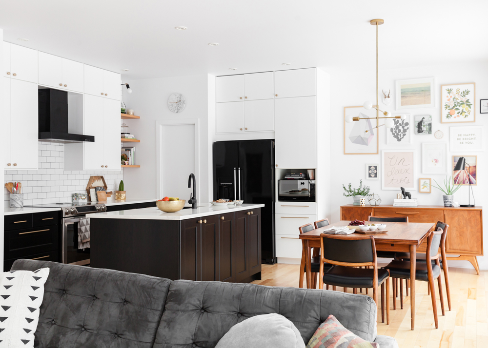 open plan kitchen with white upper cabinets, black fridge, teak dining area