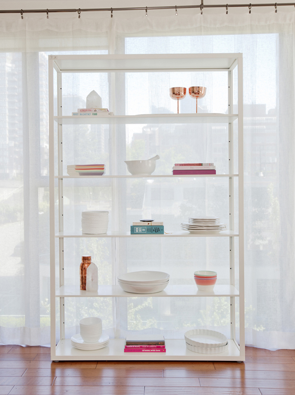 A white shelf with organized stacks of plates, cups and cookbooks