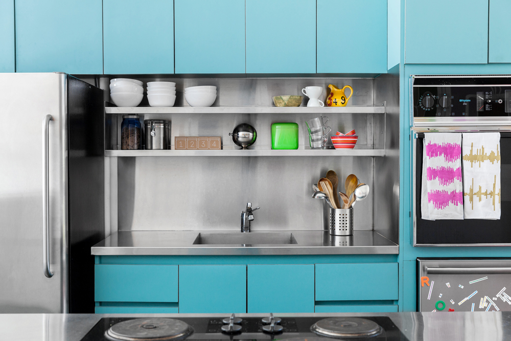 A quirky, well-lit kitchen with turquoise cabinetry and steel appliances and countertops