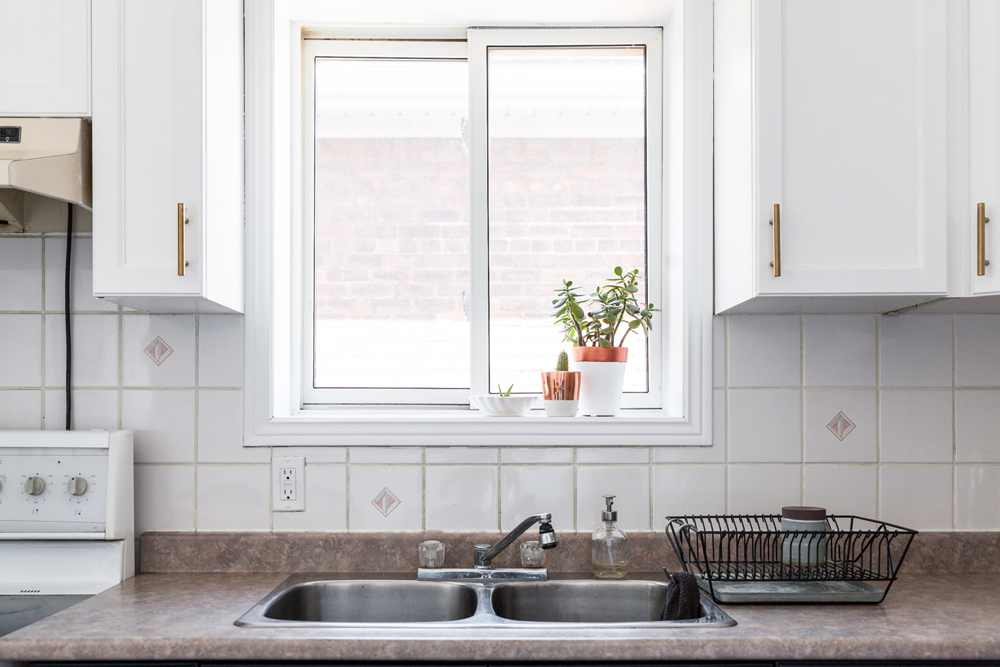 A clean kitchen counter and sink area with plants on the windowsill
