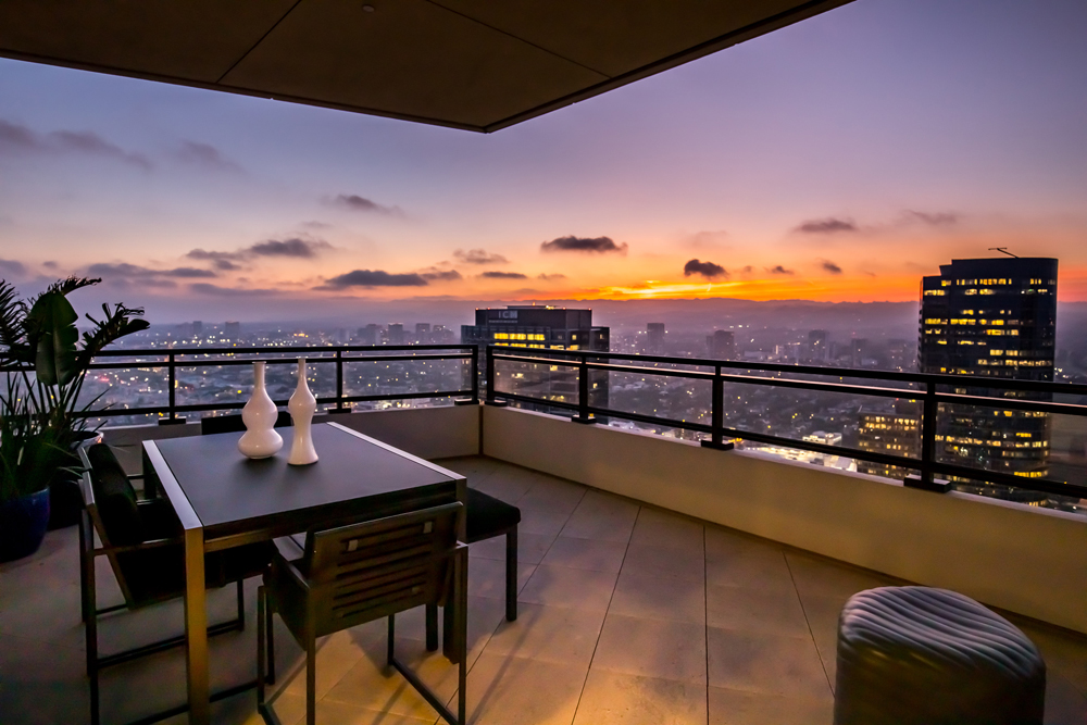 A spacious balcony with minimal furniture overlooking the Los Angeles skyline at sunset