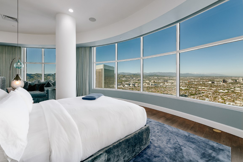 A bright master bedroom overlooking the city skyline with a plush blue area rug